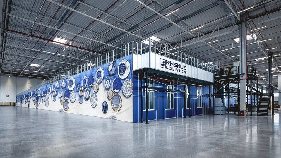 AutoStore-unit met blauwe muurdecoratie en Rhenus Logistics-logo in magazijn.