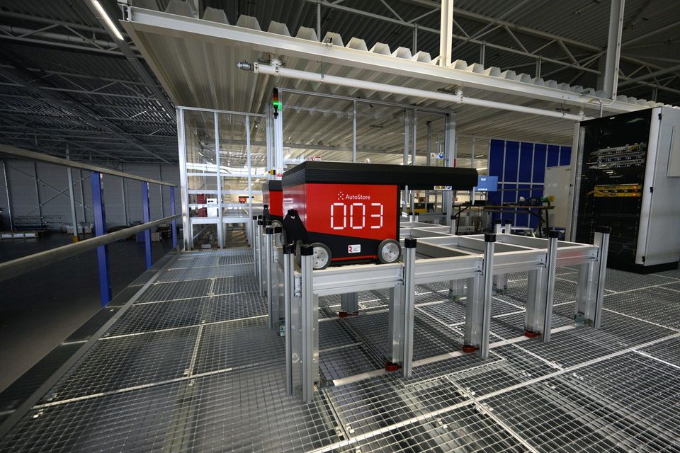 Rode AutoStore-robot nummer 003 op een magazijngrid in een distributiehal.