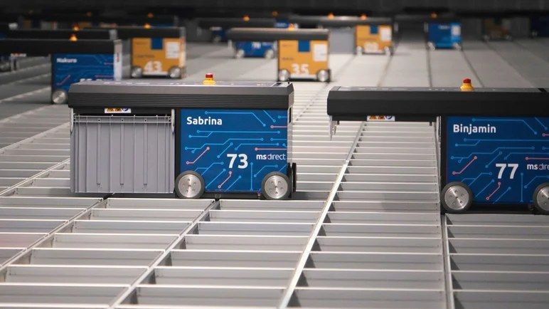 Meerdere AutoStore-robots met MS Direct-branding rijden over een metalen grid.