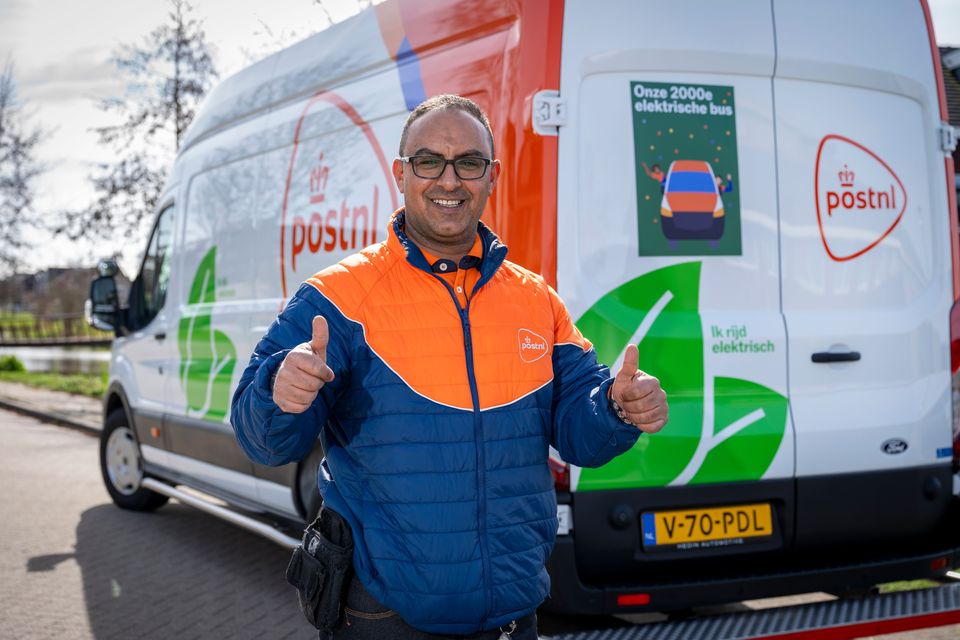 PostNL-bezorger met duimen omhoog voor elektrische bestelbus met mijlpaaksticker.