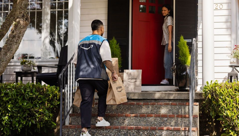 Amazon-bezorger loopt trap op met Prime-tassen naar voordeur.