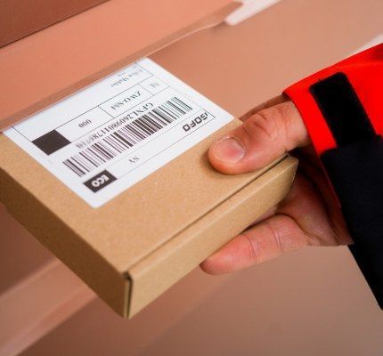 Hand in rood jasje schuift klein pakket met verzendlabel door brievenbus.