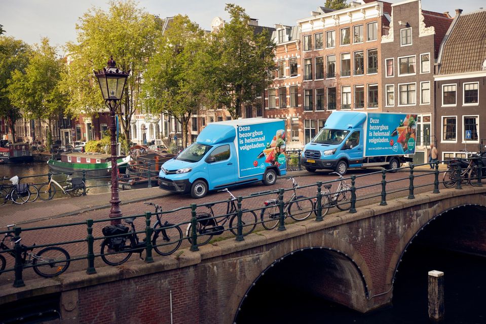 Twee blauwe bezorgbussen op een Amsterdamse grachtenbrug.