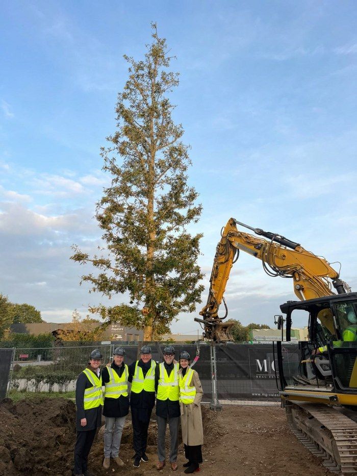 Groep mensen voor geplante boom op bouwterrein Sint-Katelijne-Waver.