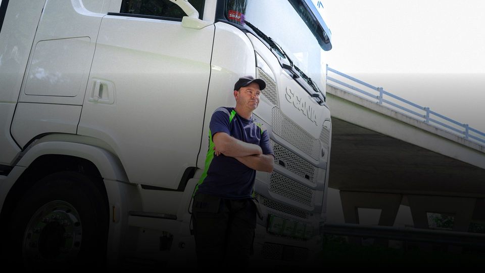 Chauffeur met gekruiste armen leunend tegen witte Scania vrachtwagen.