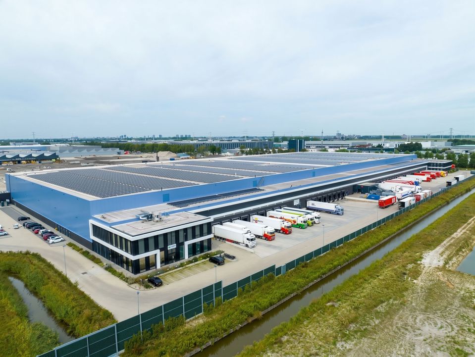 Luchtfoto van distributiecentrum met zonnepanelen en vrachtwagens bij laaddocks.