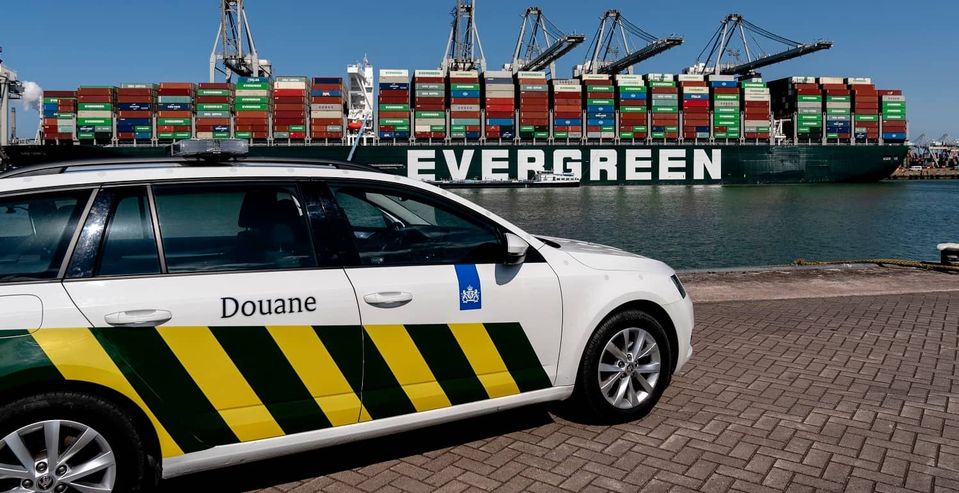 Douaneauto op havenkade voor groot containerschip met containers.