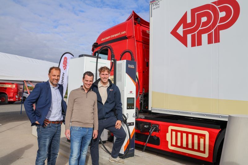 Drie mannen poseren bij een laadpaal naast een elektrische vrachtwagen.