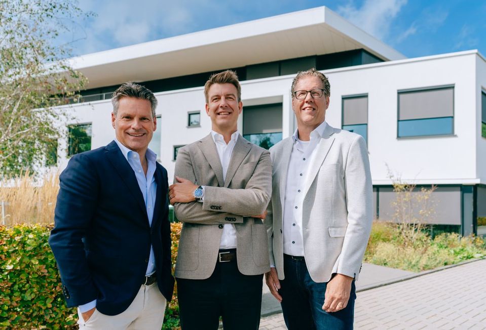 Drie mannen in zakelijke kleding poseren voor een modern wit gebouw.