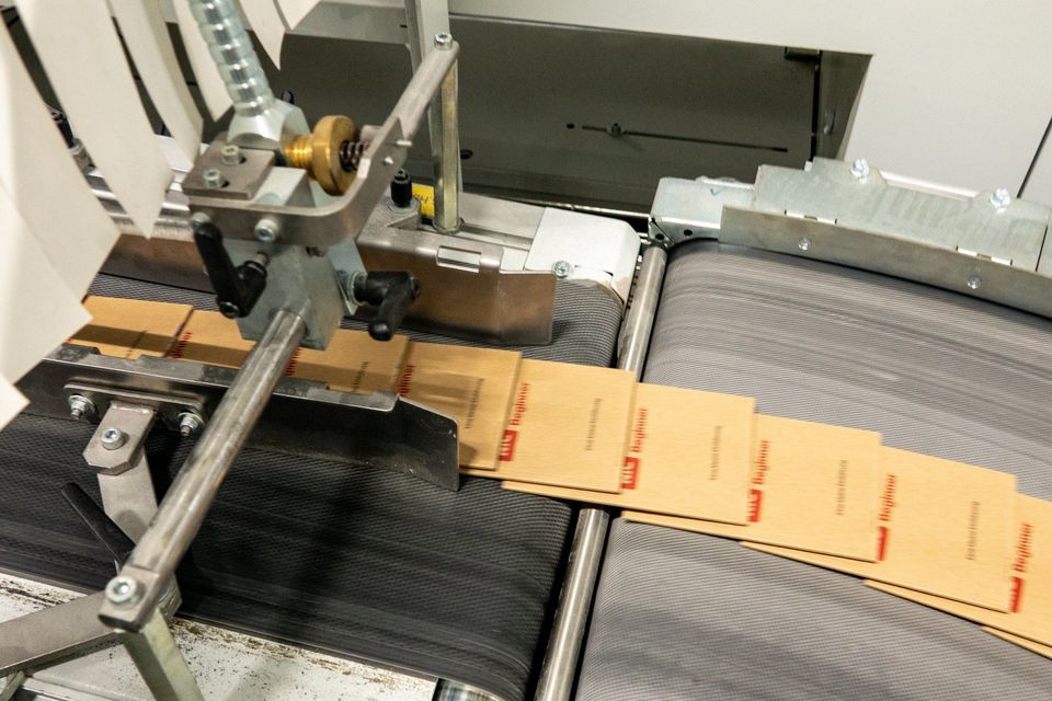 Gedrukte vellen op transportband onder industriële snij- of vouwmachine.