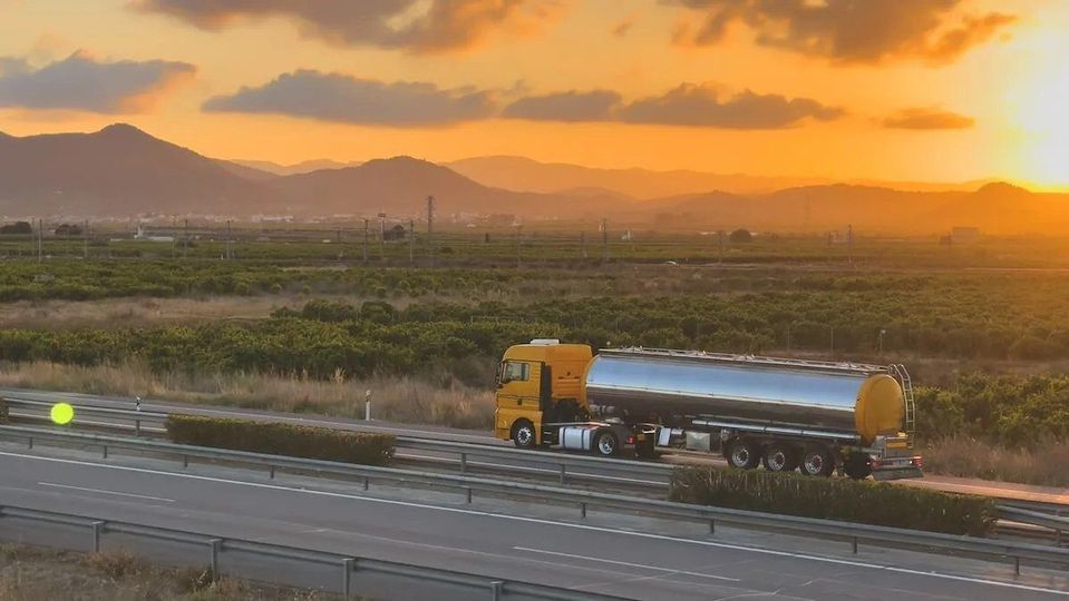 Gele tankwagen met zilveren trailer op snelweg bij zonsondergang.