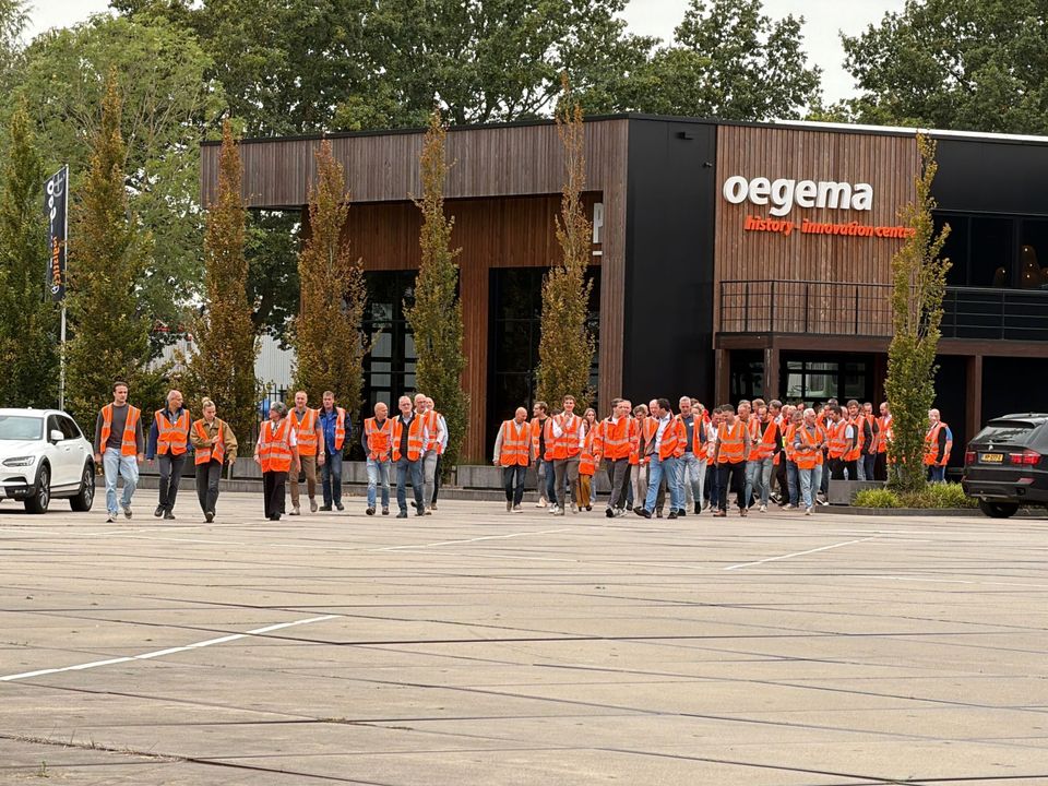 Groep mensen in oranje veiligheidshesjes voor het Oegema-gebouw in Dedemsvaart.