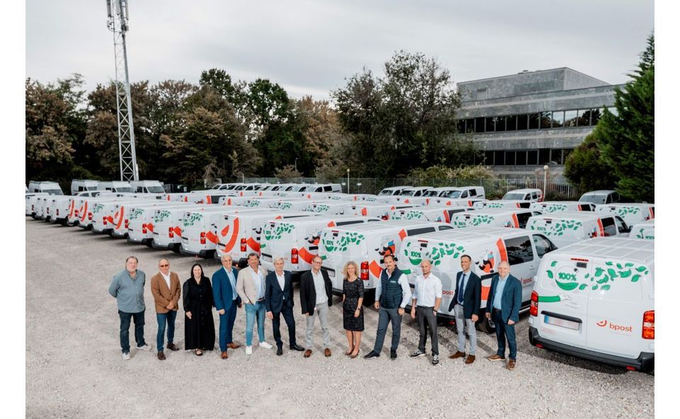 Groep mensen poseert voor rijen witte elektrische bpost-bestelbussen op parkeerplaats.