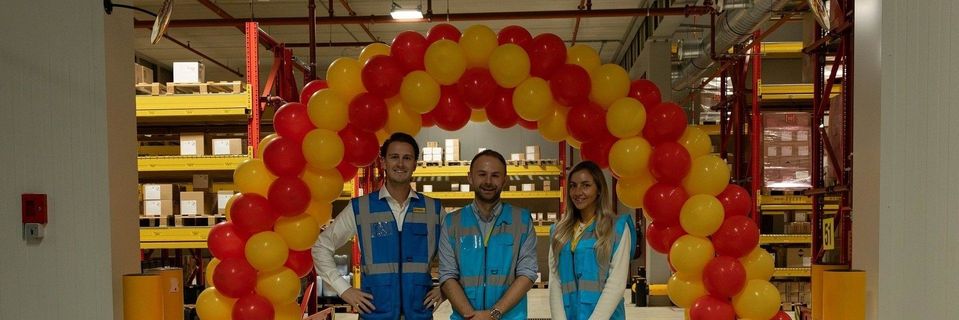 Drie personen in veiligheidsvesten onder ballonnenboog in magazijn.