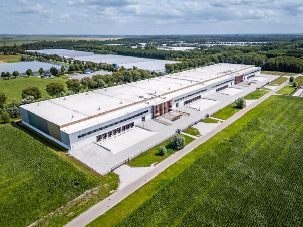 Luchtfoto van een groot wit distributiecentrum omringd door weilanden.