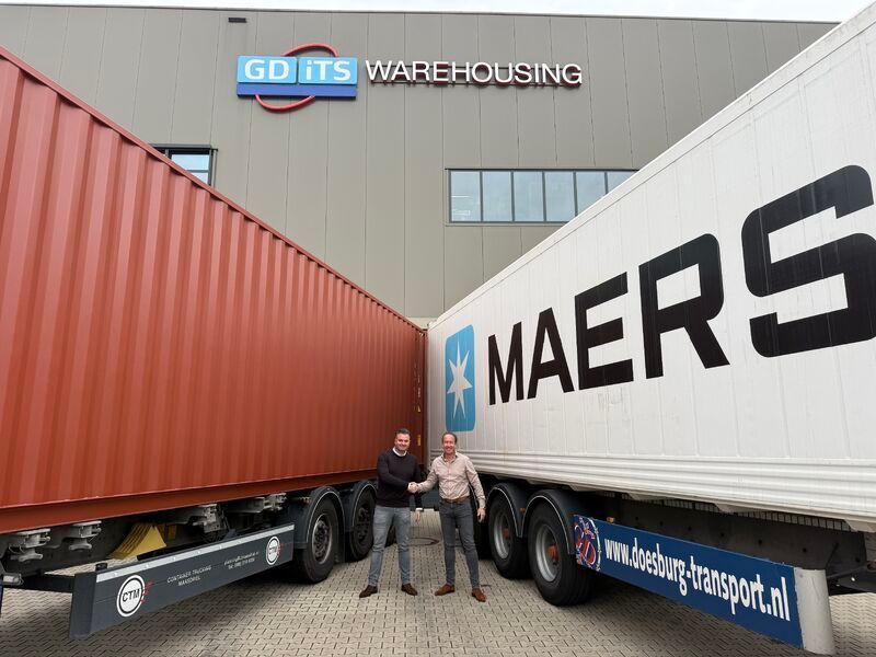 Twee mannen schudden handen tussen container en Maersk-trailer voor magazijn.