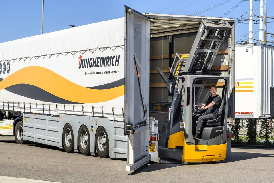 Bestuurder rijdt gele Jungheinrich heftruck uit open vrachtwagenaanhanger.