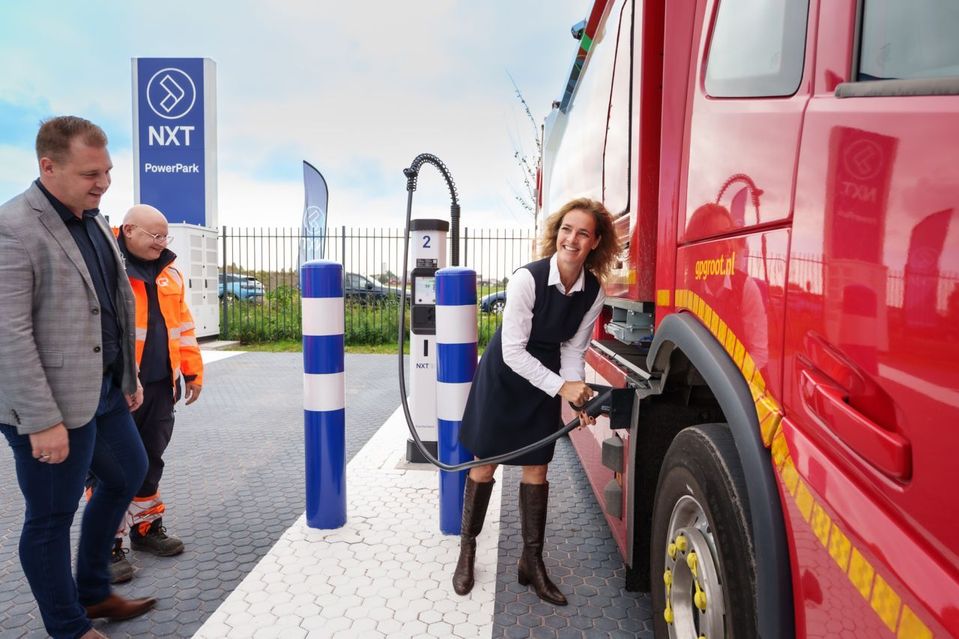 Vrouw sluit laadkabel aan op rode elektrische vrachtwagen bij NXT PowerPark.