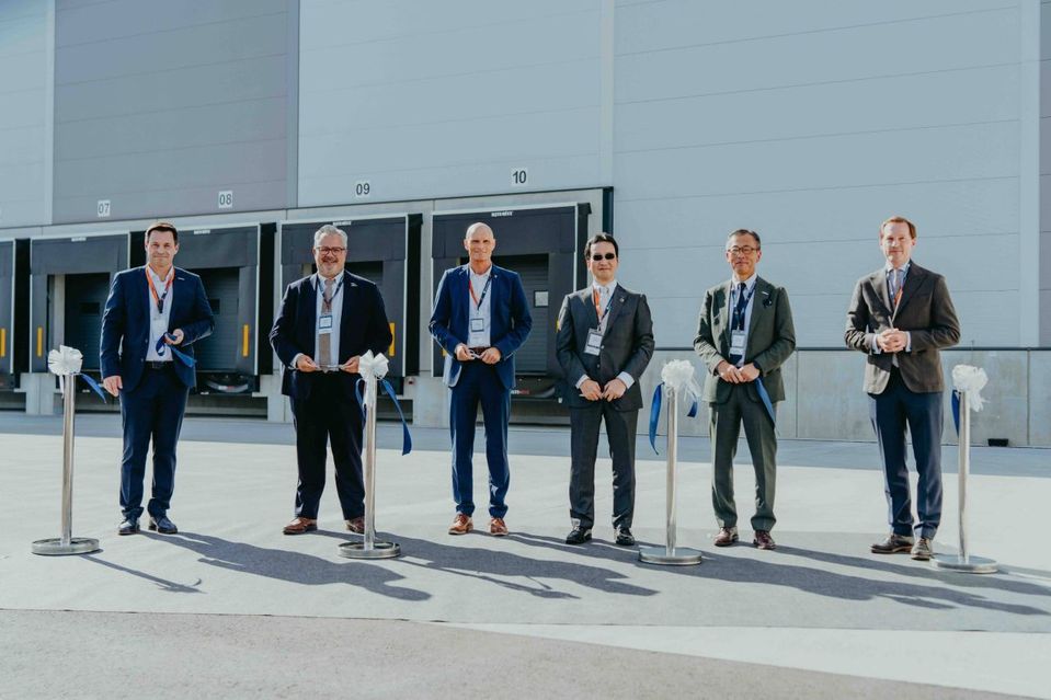 Zes personen bij lintjesceremonie voor distributiecentrum met laaddocks.