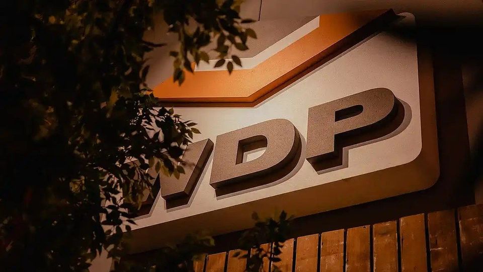 WDP-logo op een verlicht gevelbordje tussen bladeren in avondlicht.
