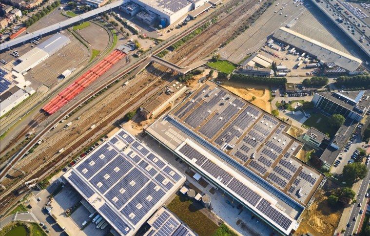 Luchtfoto van distributiecentrum met zonnepanelen op dak naast spoorlijn.