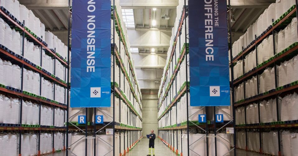 Medewerker staat tussen hoge rekken met big bags in magazijn.