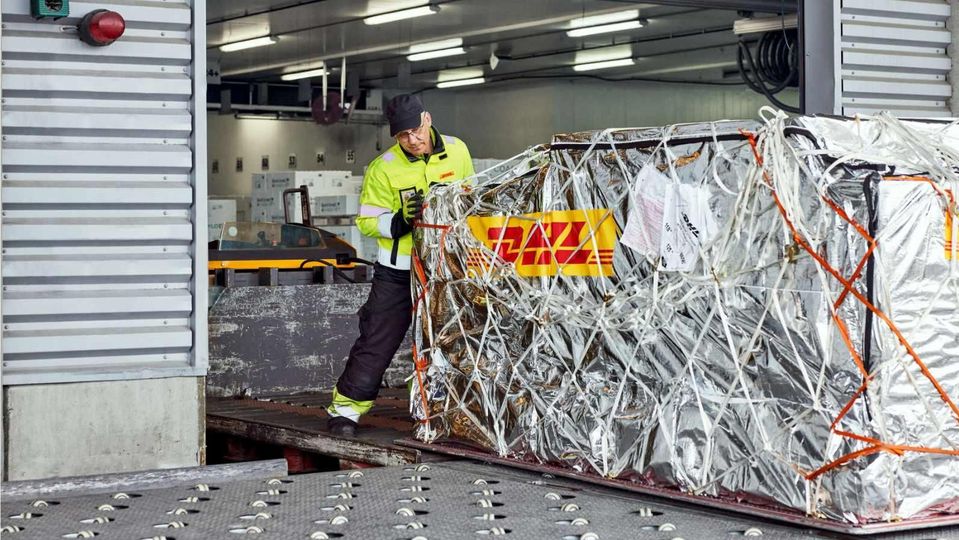 DHL-medewerker duwt met thermische deken omwikkelde luchtvracht pallet.