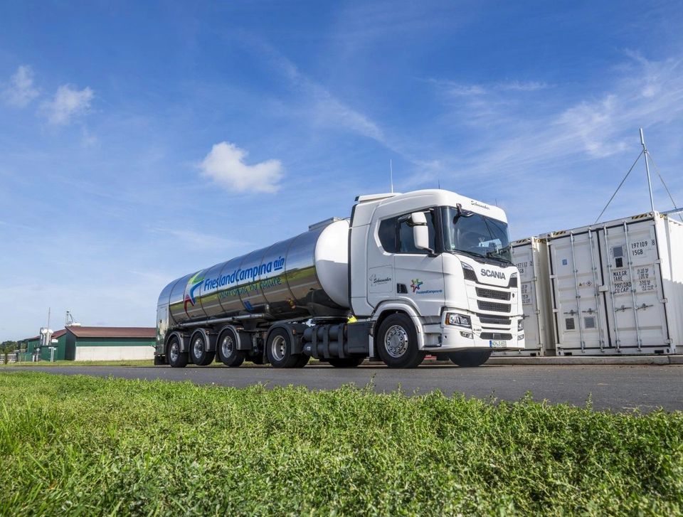 Witte Scania melktanker met zilveren tankoplegger op agrarisch terrein.
