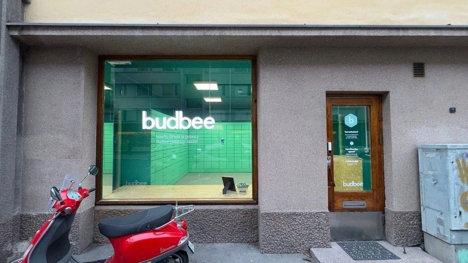 Budbee-afhaalpunt met groene pakketkluizen zichtbaar achter grote etalageruit.