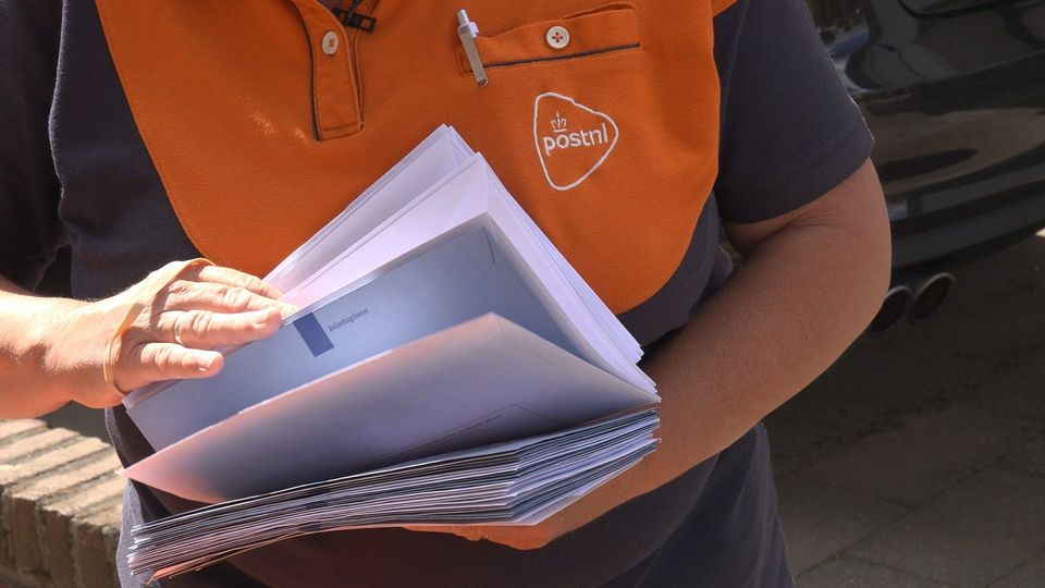 PostNL-bezorger in oranje uniform met stapel brieven in hand.