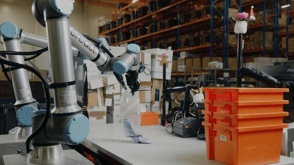 Robotarm van Sereact sorteert retourpakket naast oranje sorteerbakken in magazijn.