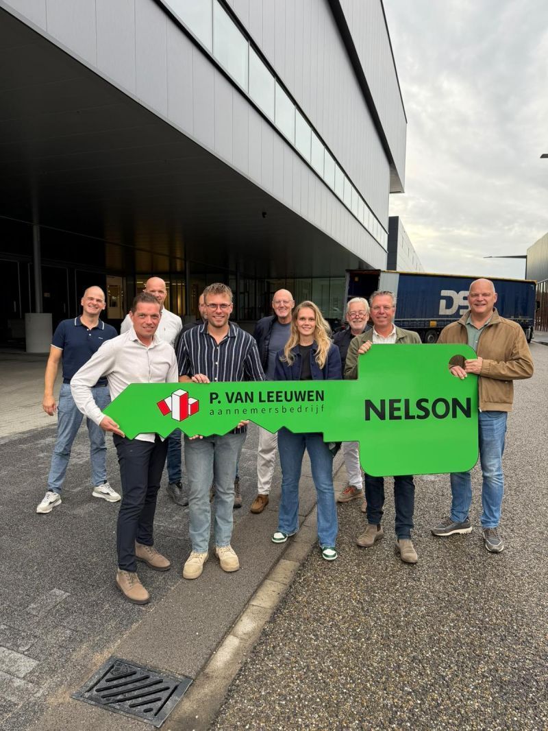 Groep mensen houdt grote groene sleutel vast voor distributiecentrum.