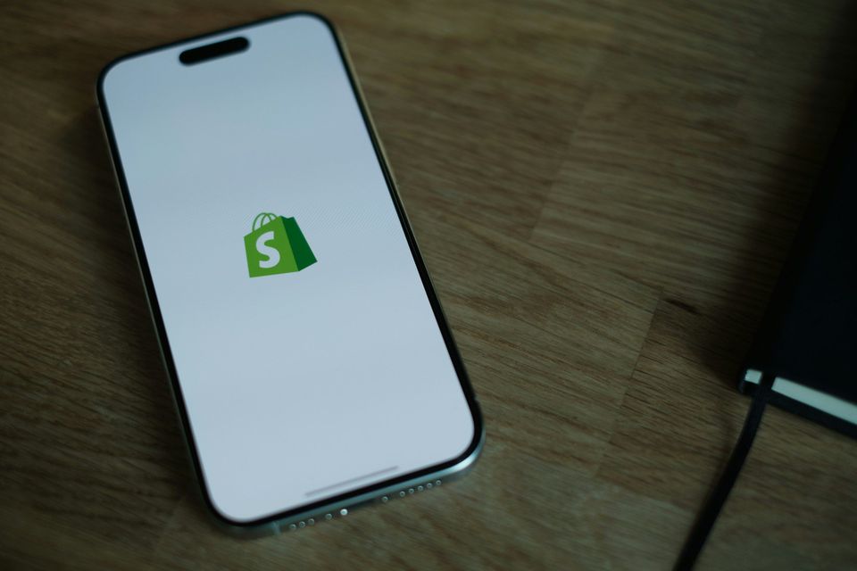 Smartphone met Shopify-logo op wit opstartscherm, liggend op houten tafel.