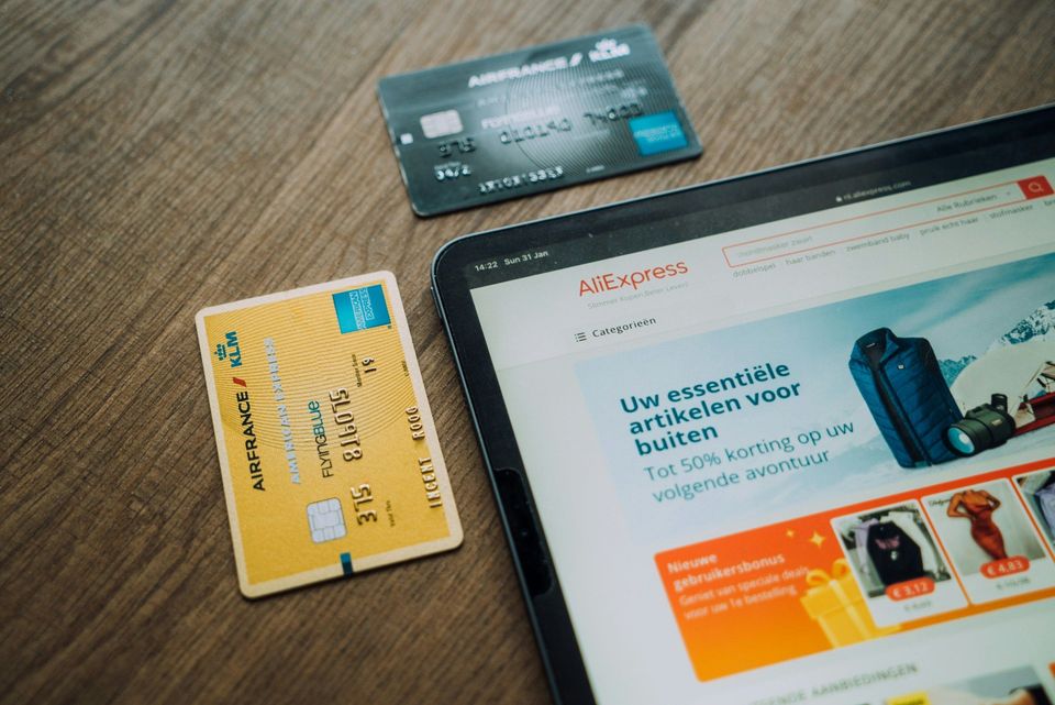 Tablet met AliExpress-website en twee betaalkaarten op houten tafel.