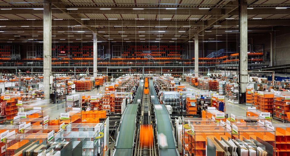 Bovenaanzicht van groot magazijn met transportbanden en oranje kratten.