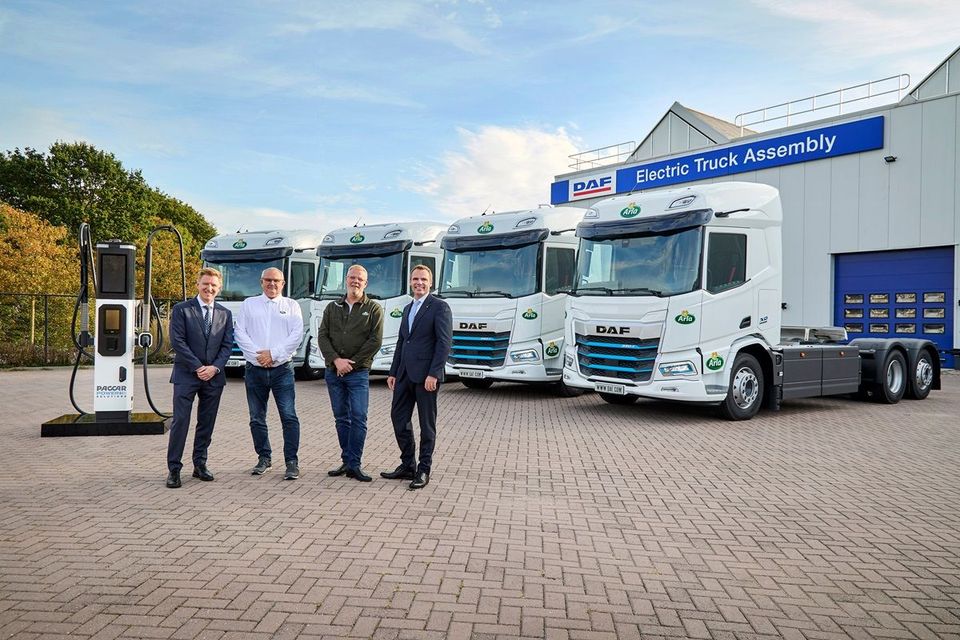 Vier personen voor witte elektrische DAF-trucks met Arla-logo en laadpaal.