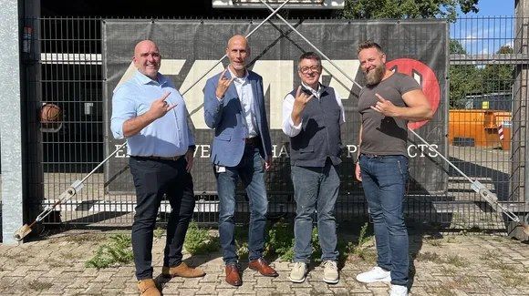 Vier mannen maken een rockgebaar voor het hek van het EMP-distributiecentrum.