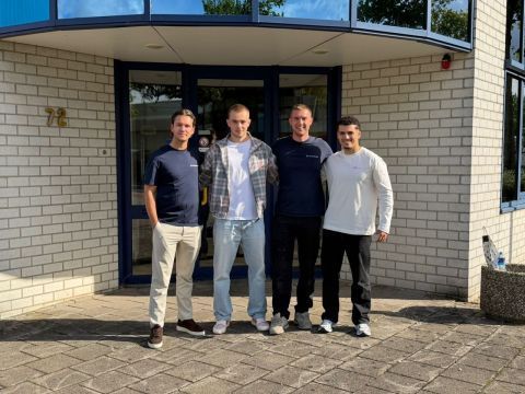 Vier mannen poseren voor de ingang van een bedrijfspand.