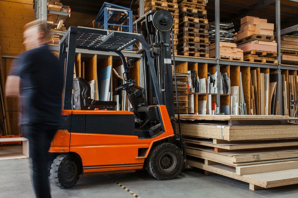 Oranje heftruck in magazijn met bewegende voetganger op de voorgrond.
