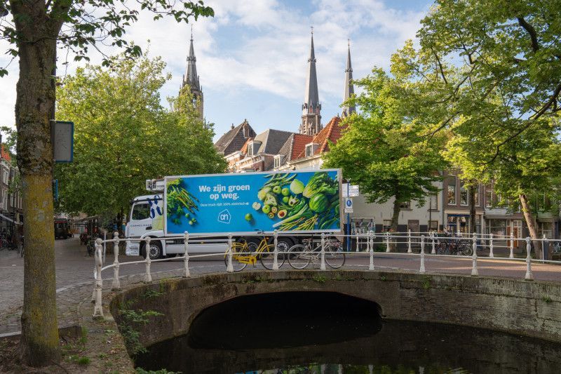 Albert Heijn vrachtwagen met groene opdruk op brug over gracht.