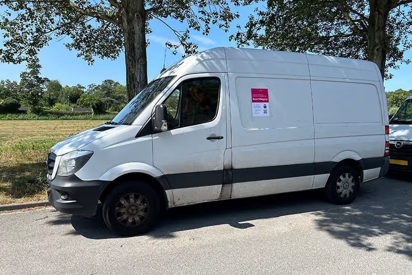 Witte bestelbus met roze stilleggingssticker geparkeerd langs de weg.